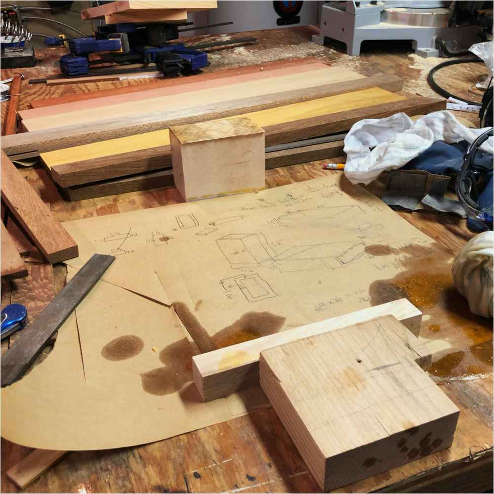 Plans for the design and dimensions of the playing card box are laid out with wood and tools surrounding it.