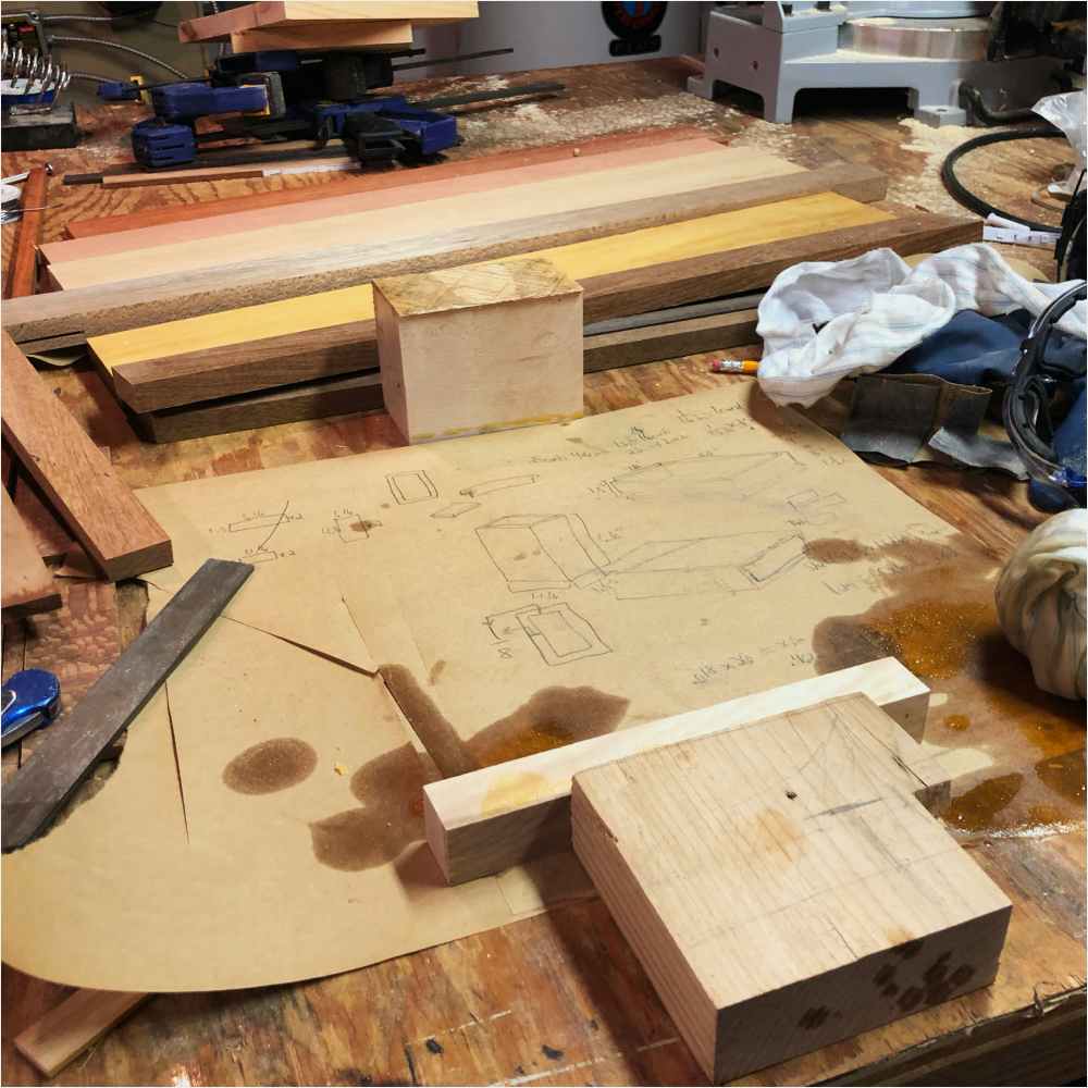 Plans for the design and dimensions of the playing card box are laid out with wood and tools surrounding it. Plans for the design and dimensions of the playing card box are laid out with wood and tools surrounding it.